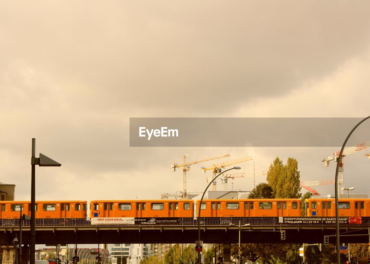 Train on railway bridge in city against cloudy sky