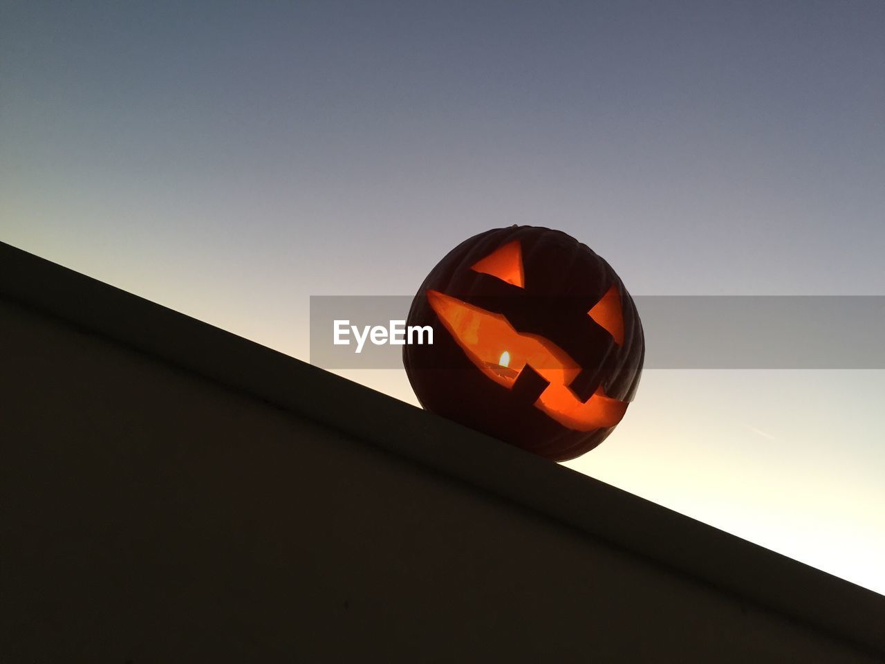 Low angle view of jack-o-lantern on retaining wall against clear sky at dusk