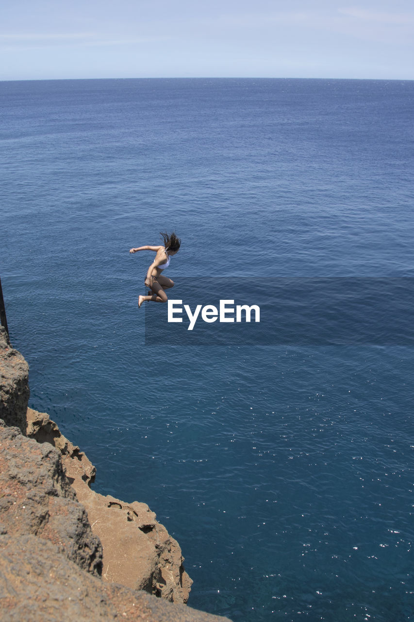 Woman jumping off cliff in sea