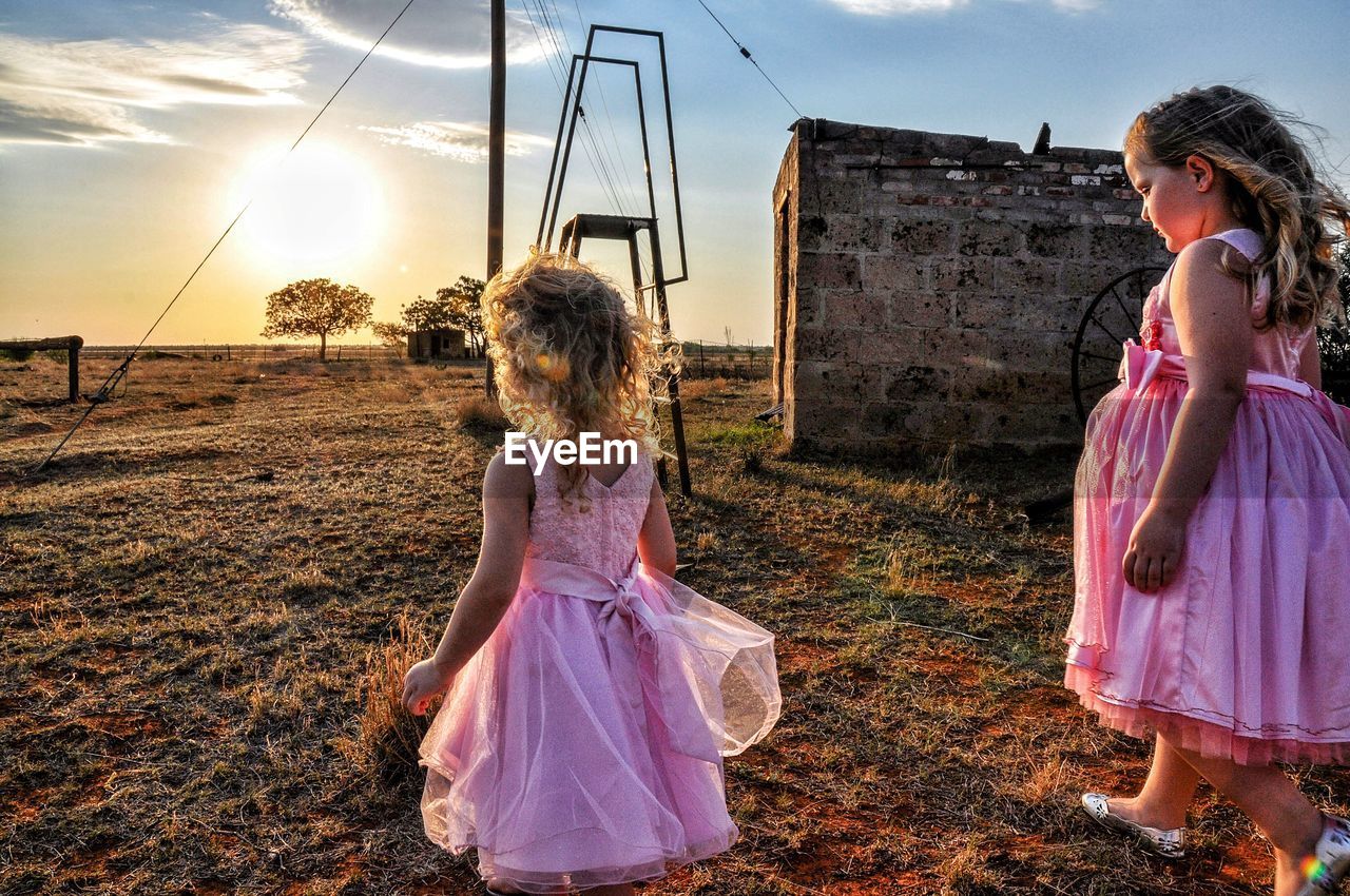 Sisters wearing pink dress while walking on field during sunset