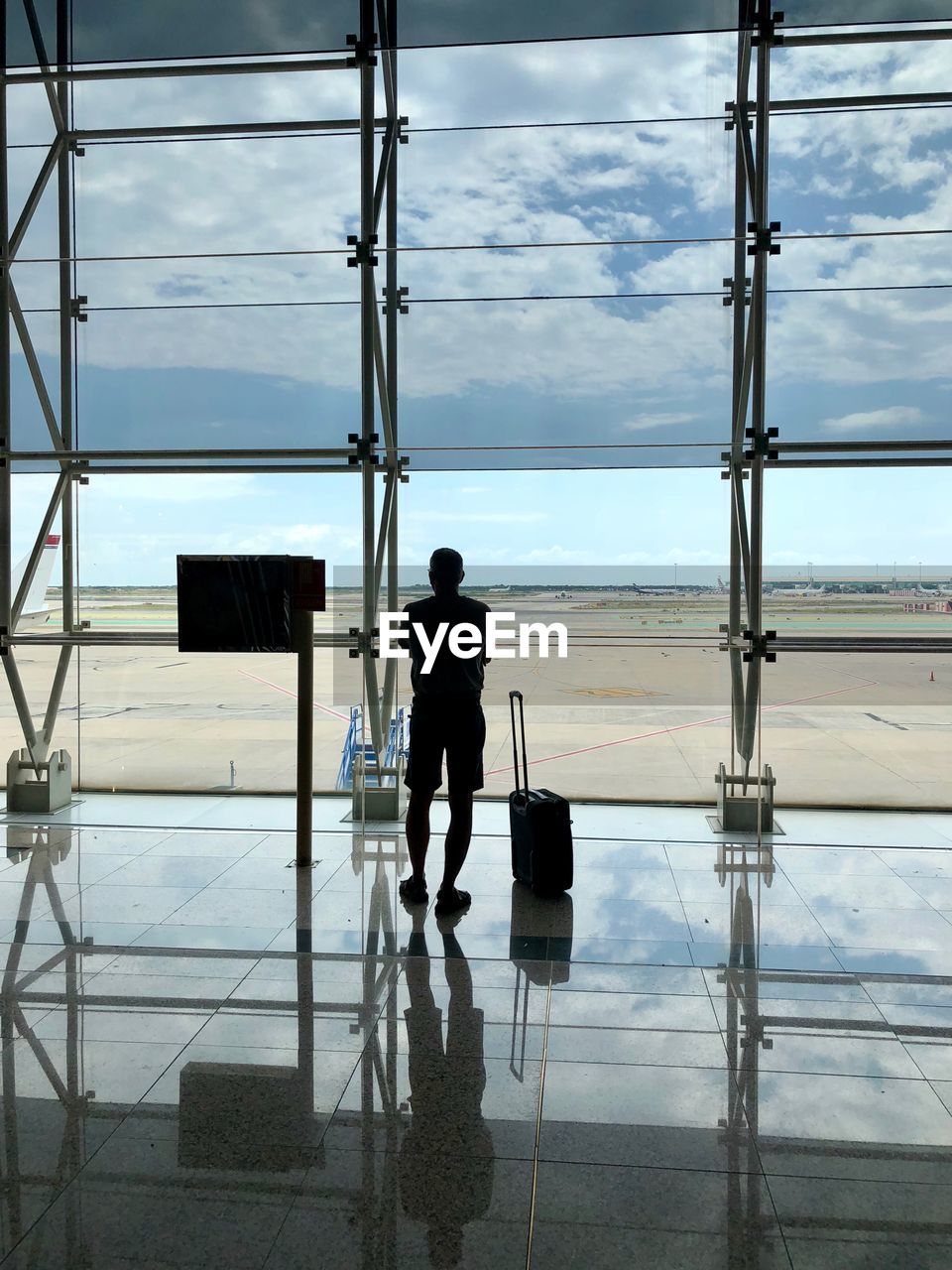 Rear view of man looking through window while standing at airport