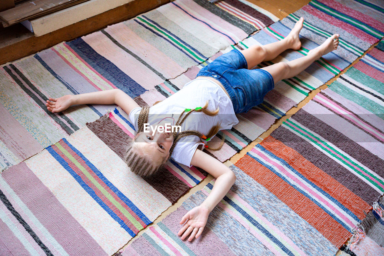 A beautiful cheerful girl with pigtails lies on the floor, on woven rugs. rest after exercise. 