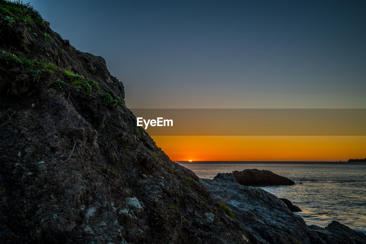 Close-up of rock by sea against sky during sunset