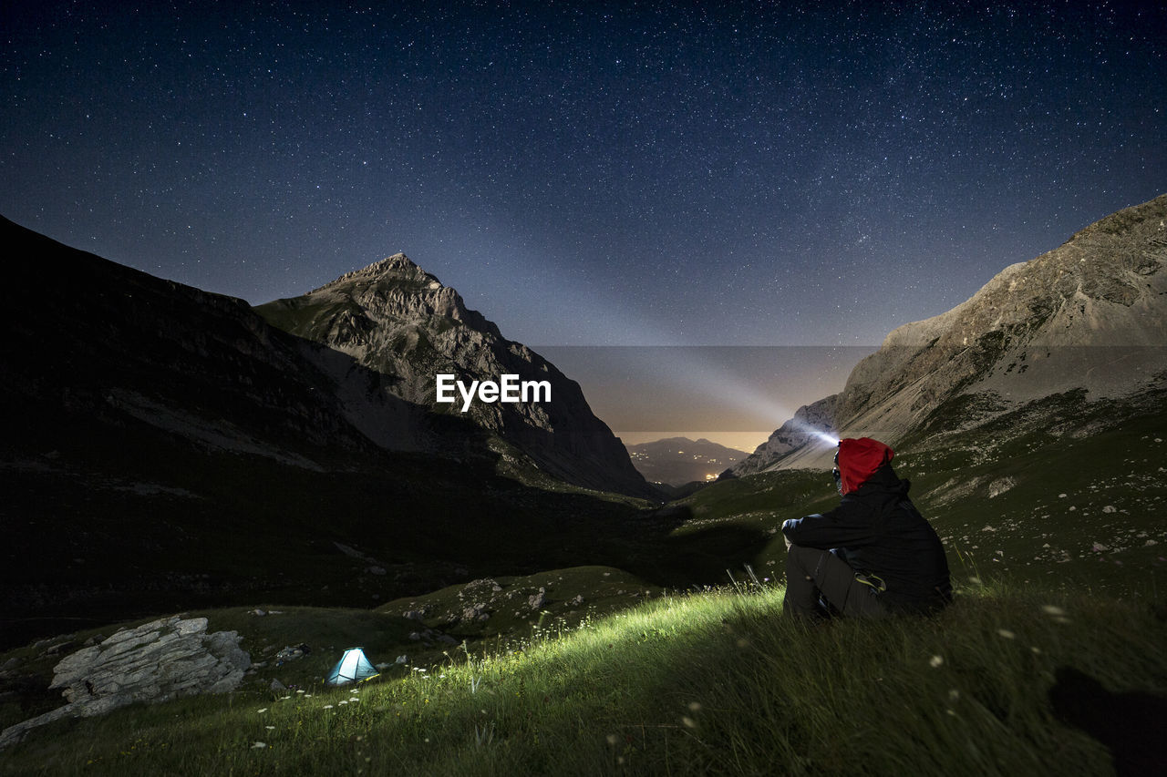 Man with flashlight sitting on mountain at night