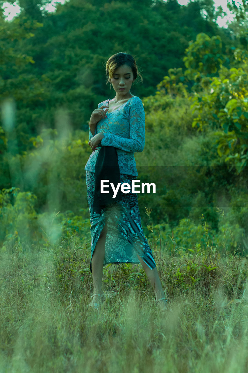 Full length of woman with traditional clothing of bali standing against the forest