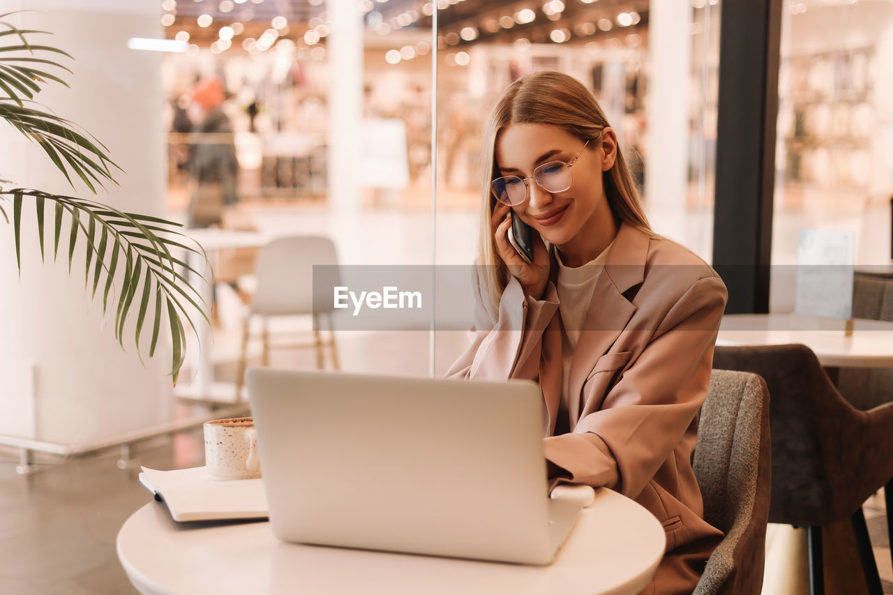 A millennial business woman with glasses works and studies using mobile phone and technology in cafe