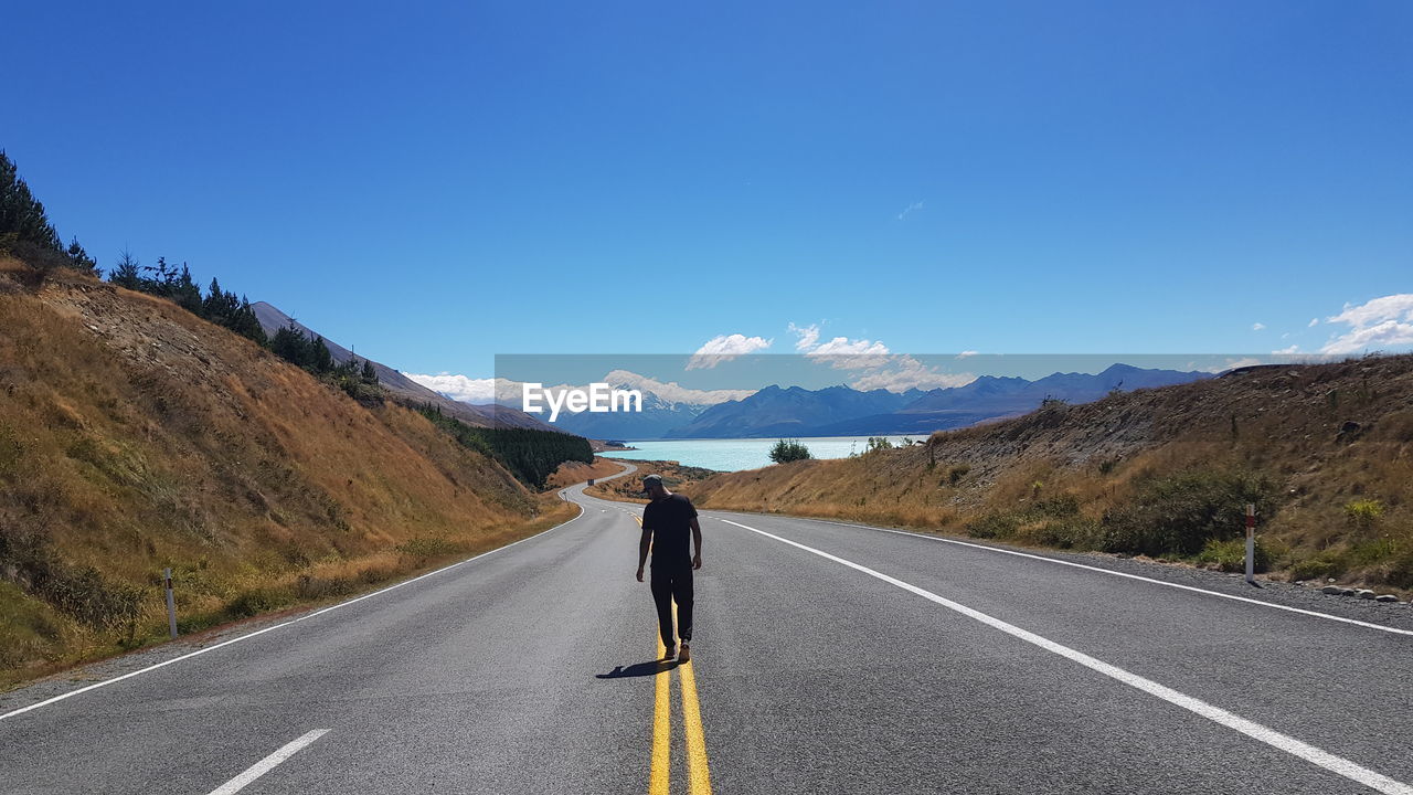 Rear view of man walking on road against clear blue sky