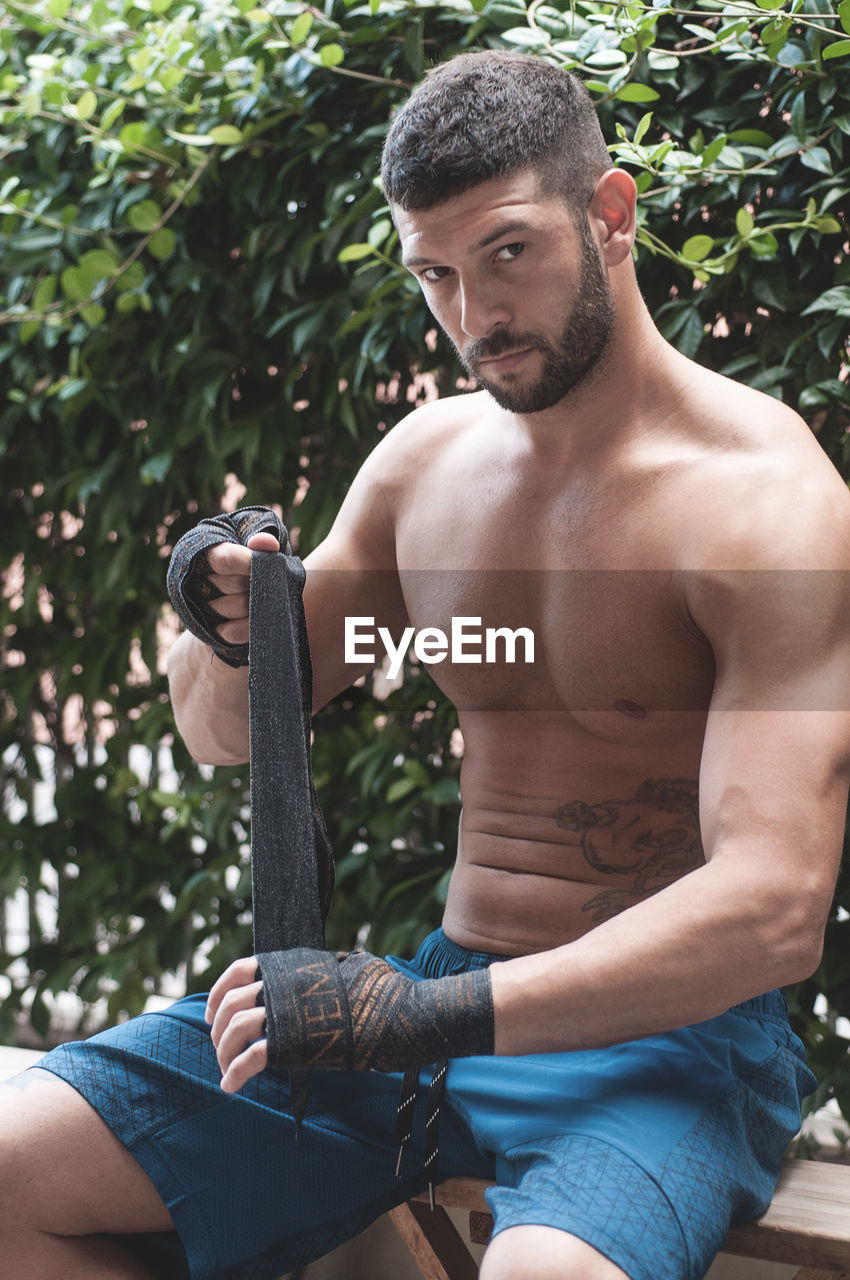 Close-up of shirtless boxer sitting against plants