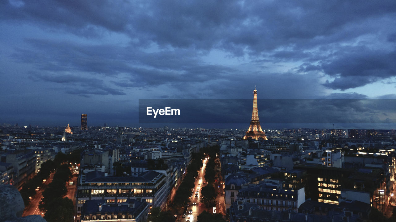 Illuminated eiffel tower amidst buildings in city against sky during sunset