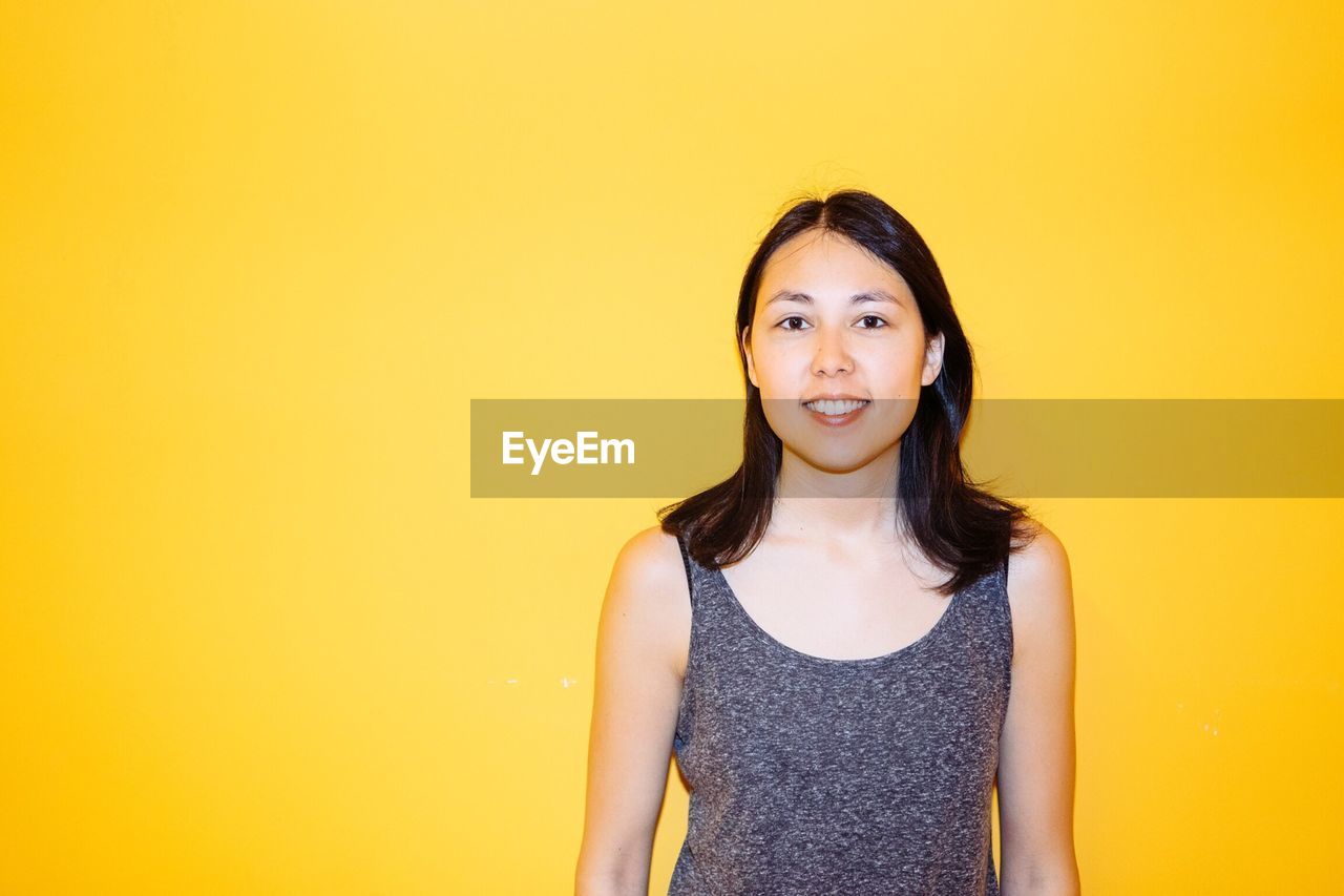 Portrait of smiling young woman against yellow background