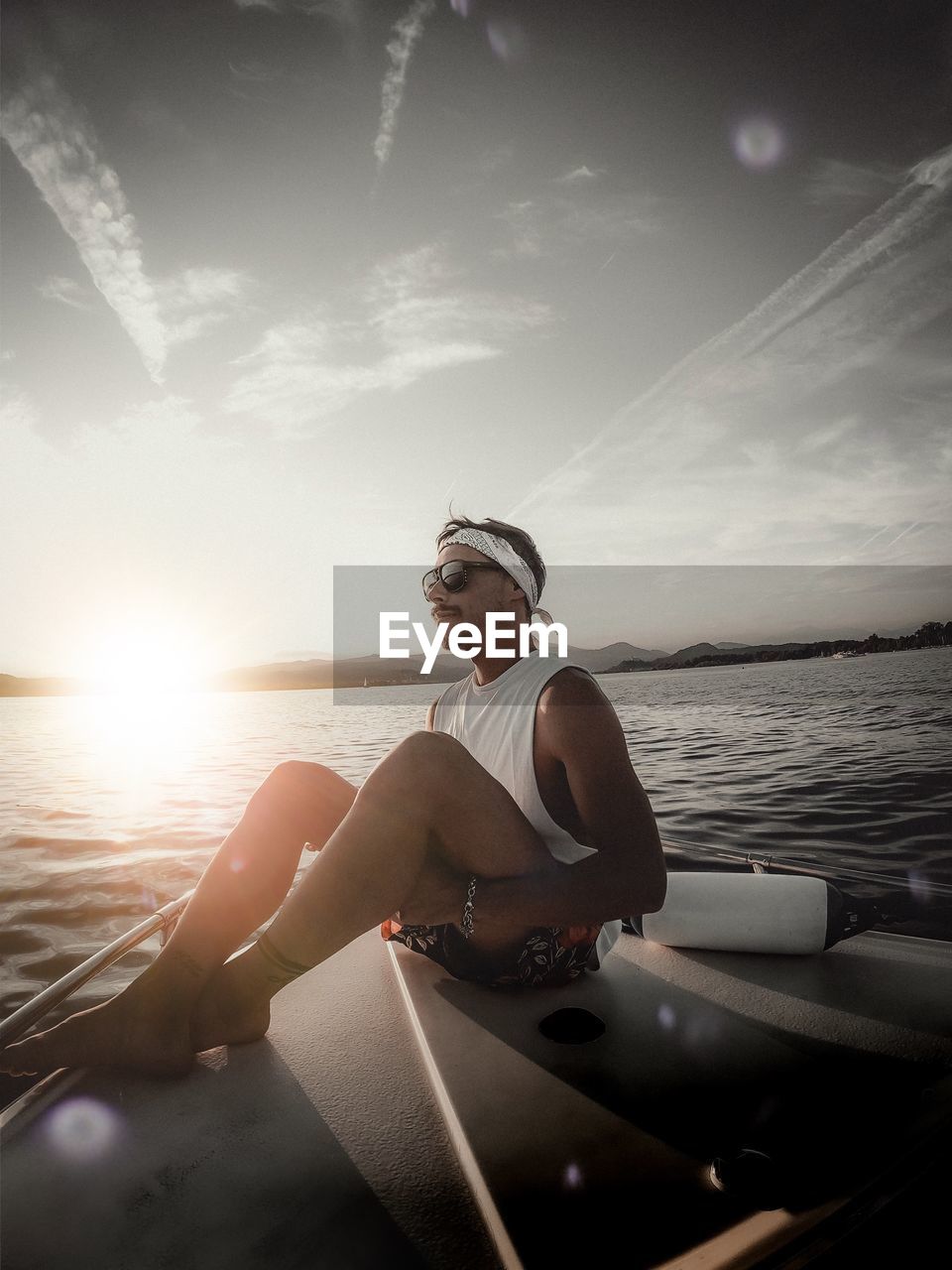 Man sitting on boat in sea against sky during sunset