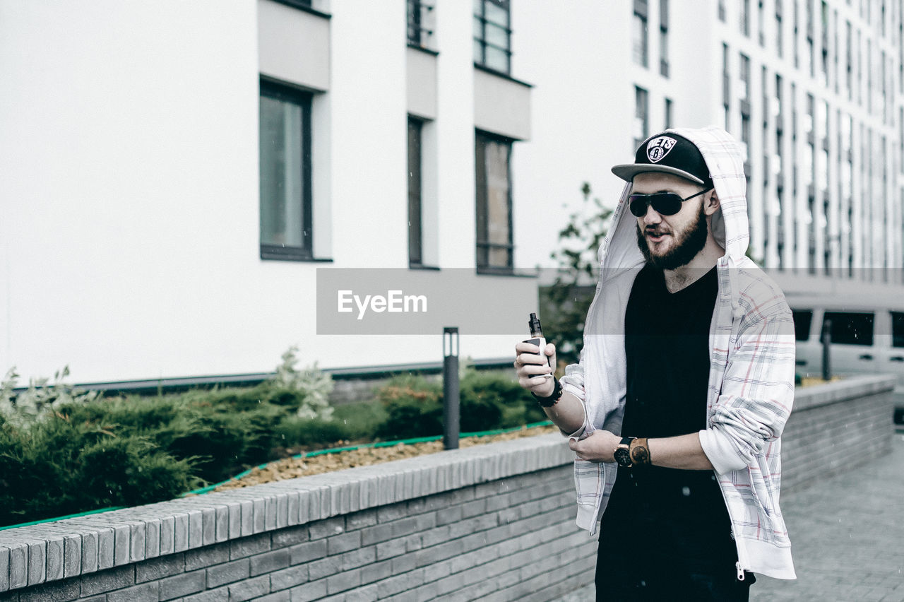 Man holding electronic cigarette while standing in city during rain