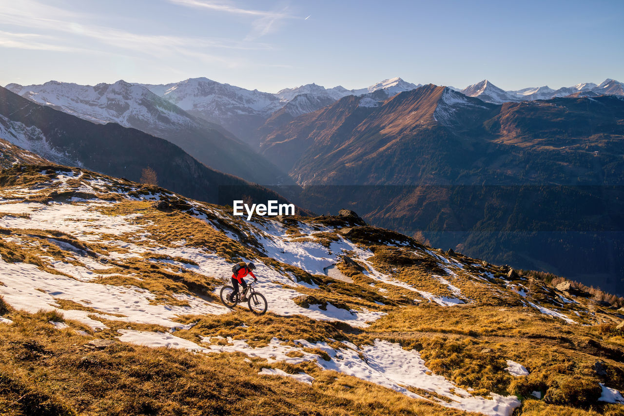 Woman riding a mountain bike on footpath in snow covered alpine terrain, gastein, salzburg, austria.