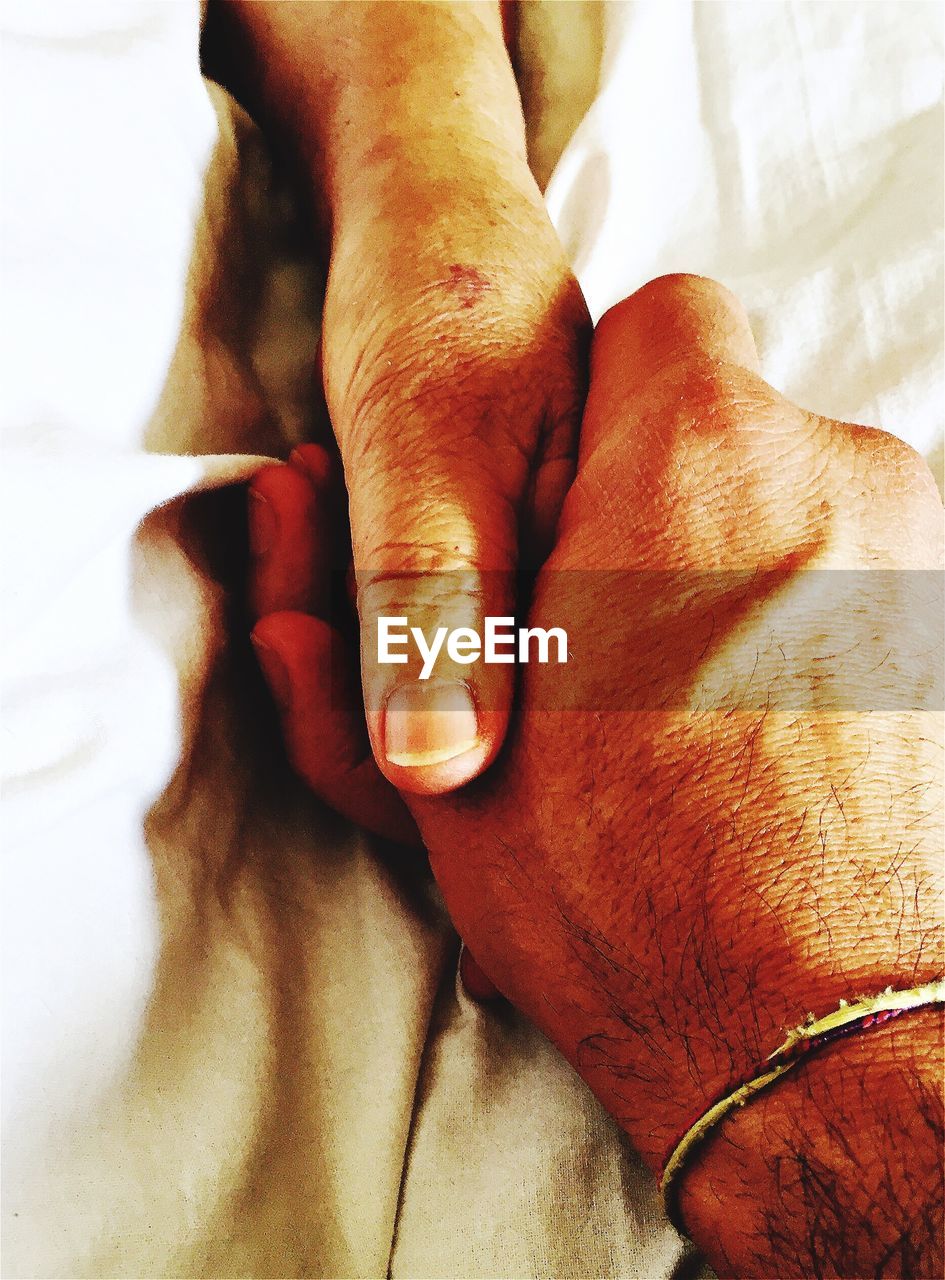 Cropped image of couple holding hands on bed
