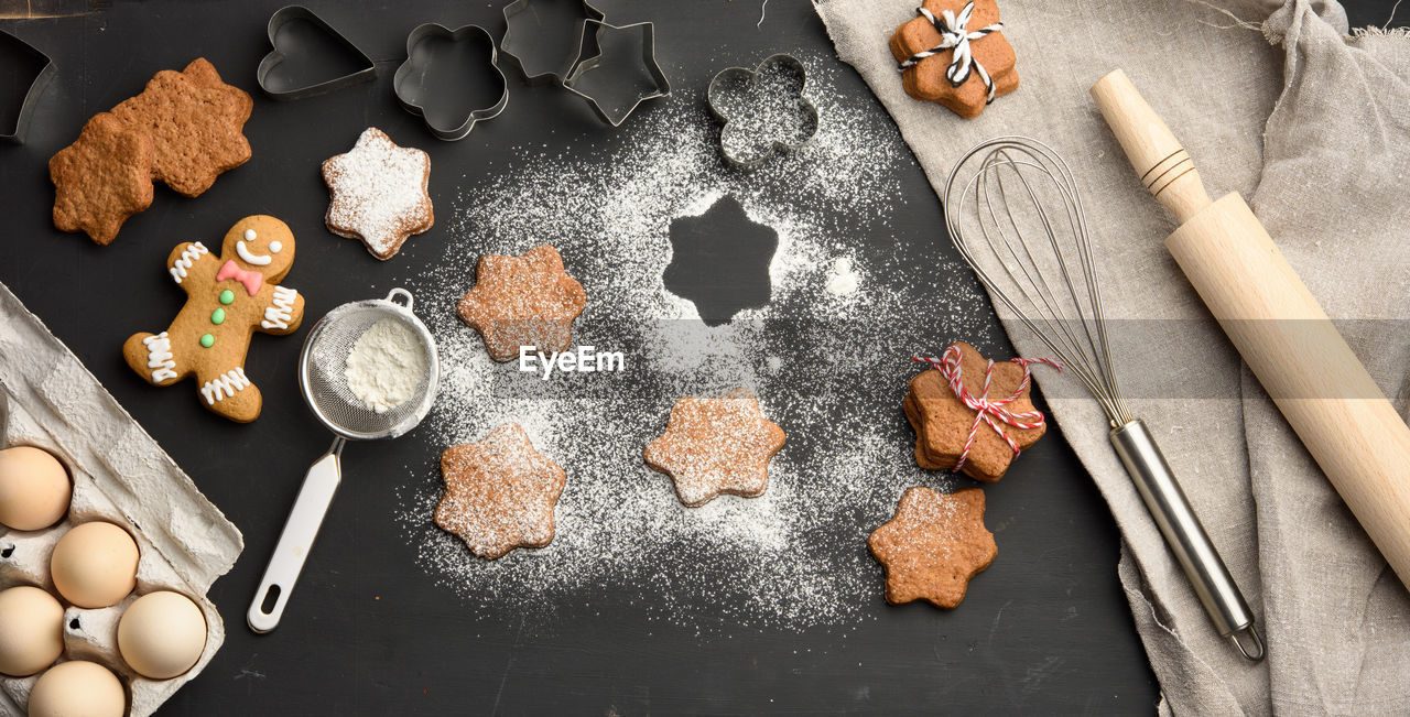 Star shaped baked gingerbread cookies sprinkled with powdered sugar on a black table, top view