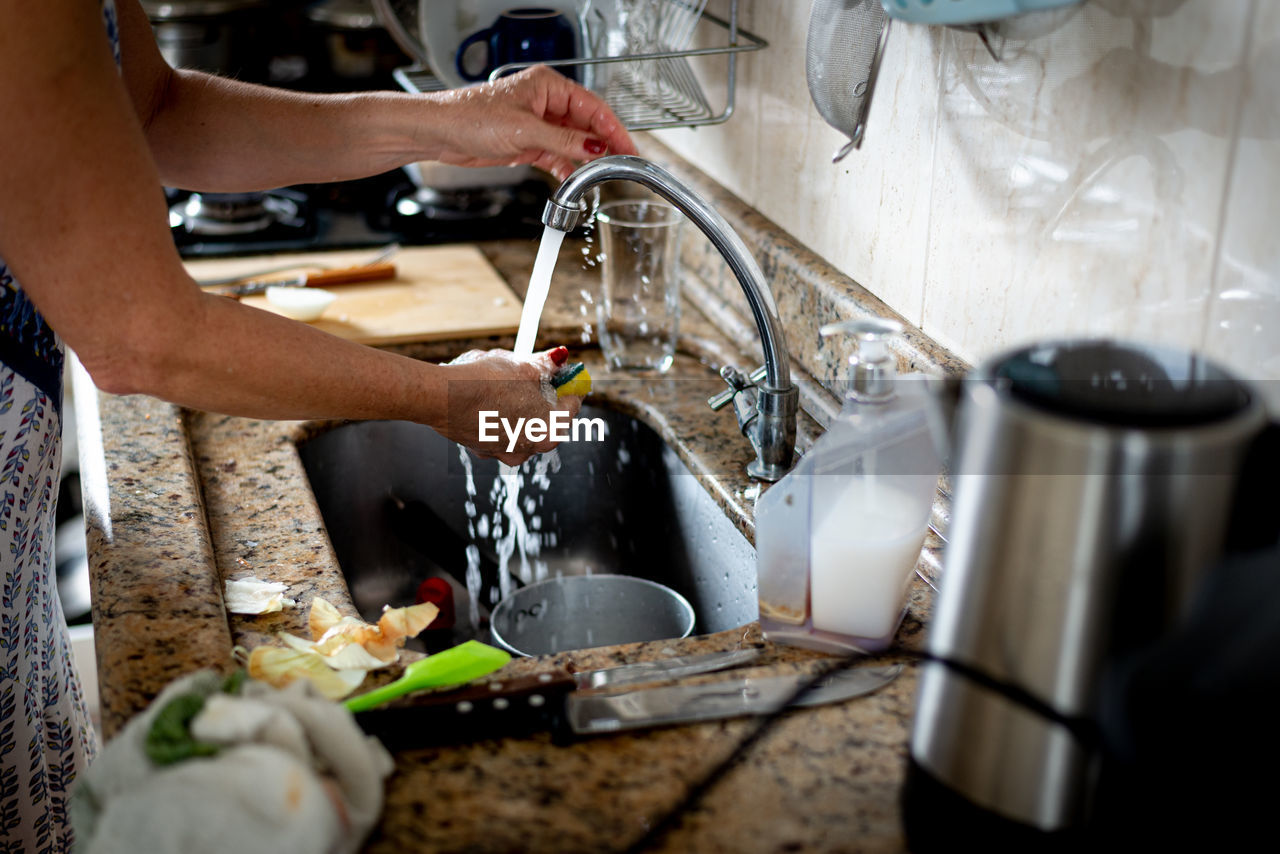 Hands of a woman washing pan in the kitchen sink.