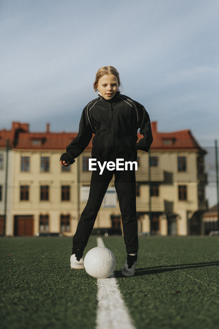 Female athlete playing with soccer ball against sky at sports field