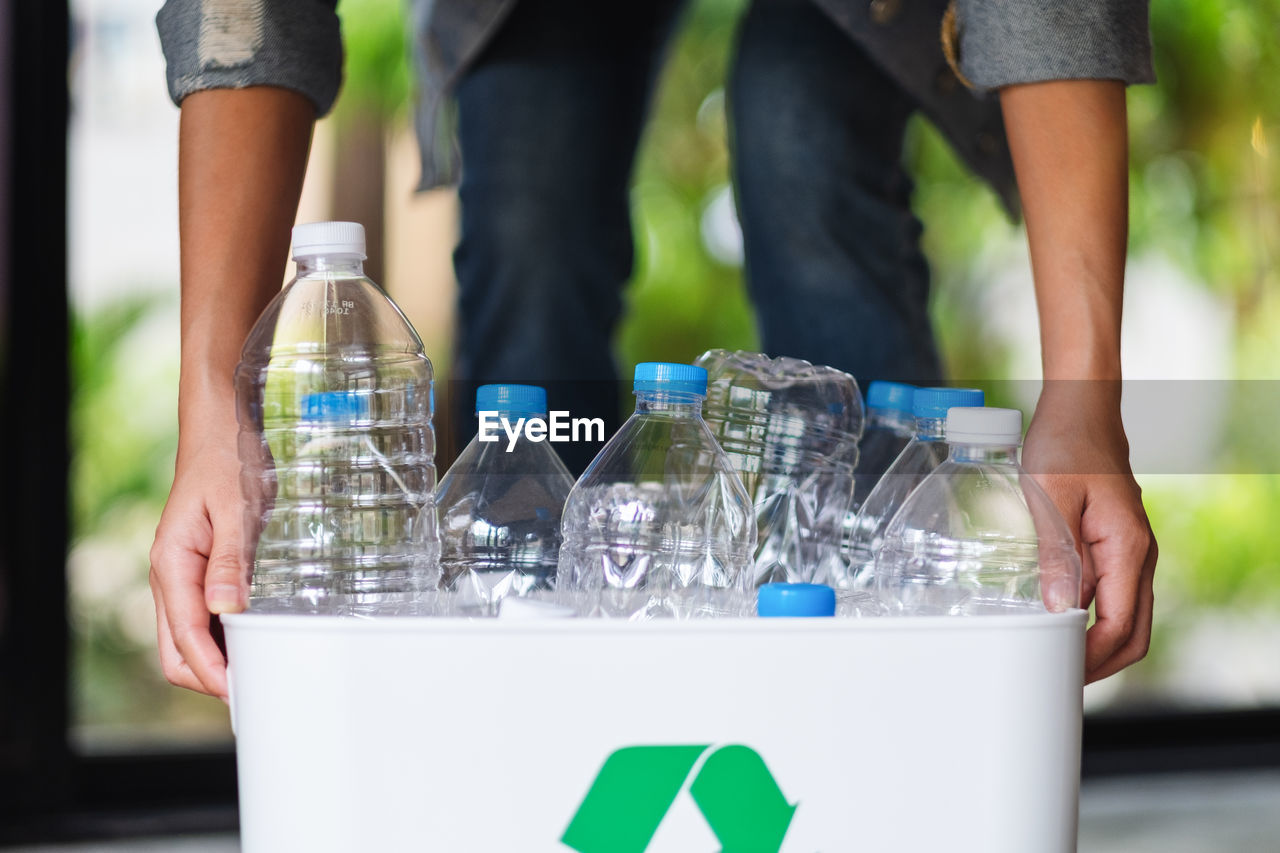 A woman collecting and holding recyclable garbage plastic bottles in a trash bin at home