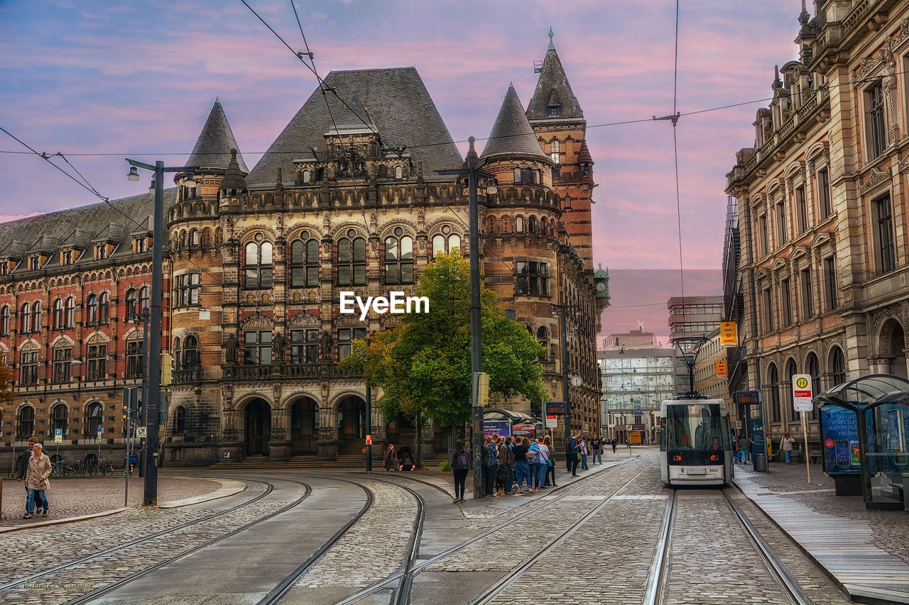 PEOPLE ON STREET AMIDST BUILDINGS IN CITY DURING SUNSET