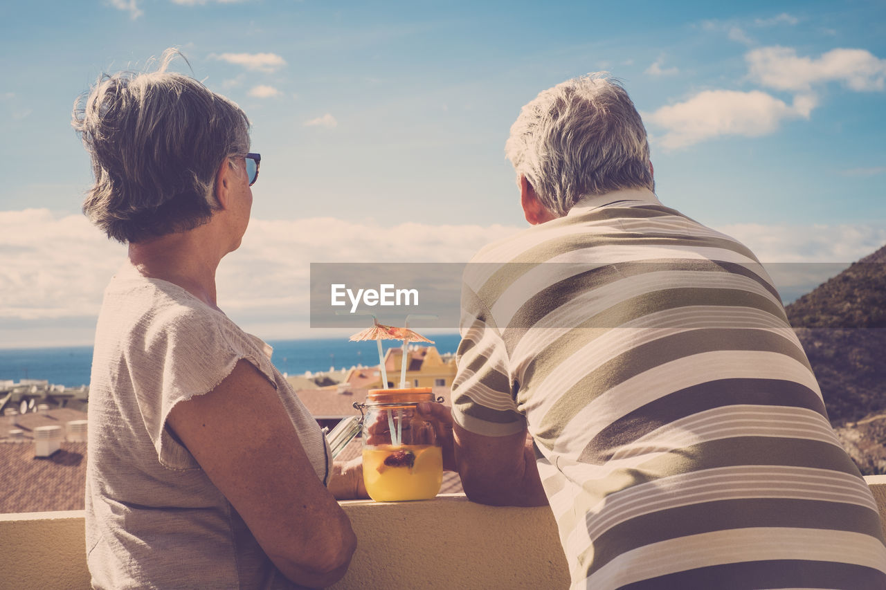 Man and woman having drink while looking at view against sky