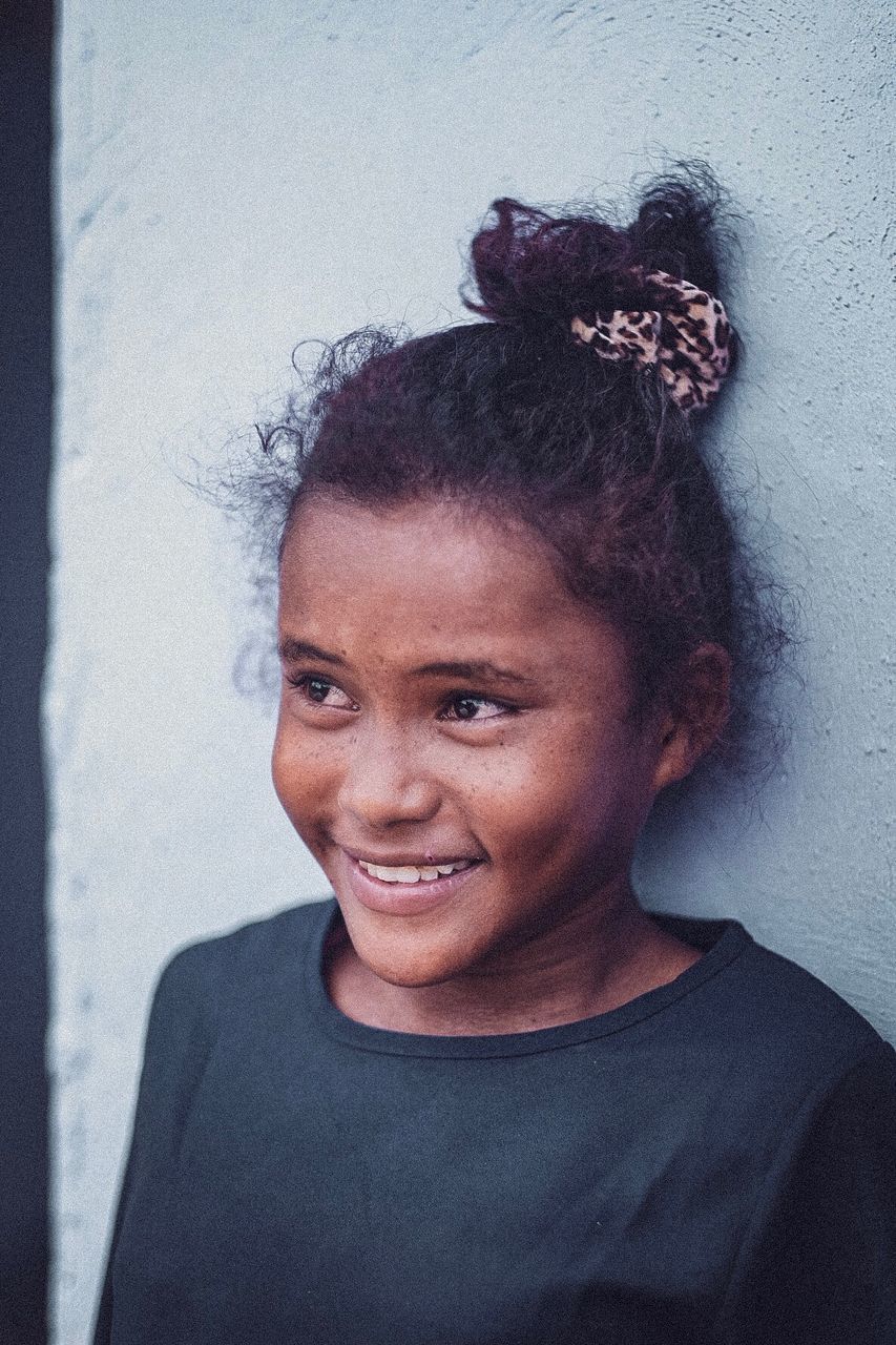 PORTRAIT OF HAPPY WOMAN STANDING AGAINST WALL