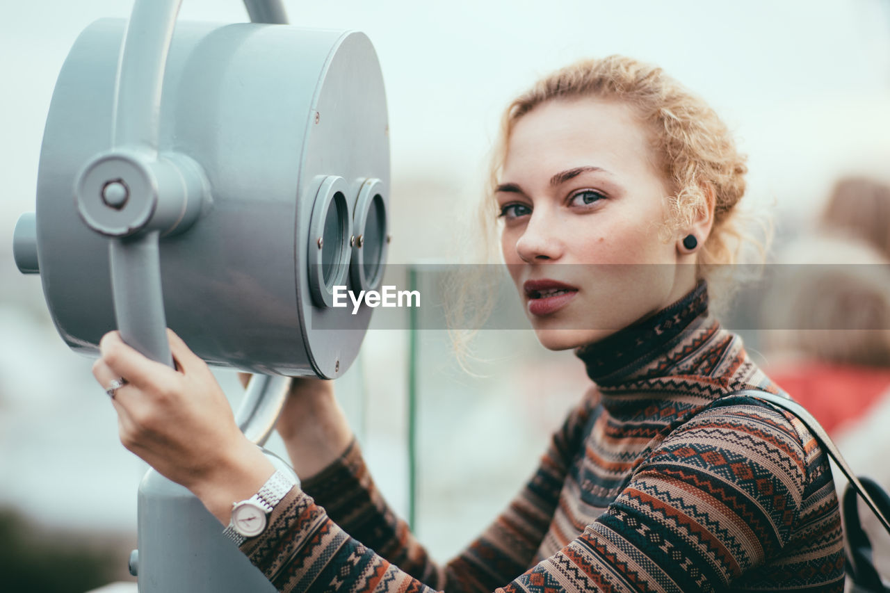 Close-up portrait of woman standing by coin-operated binoculars