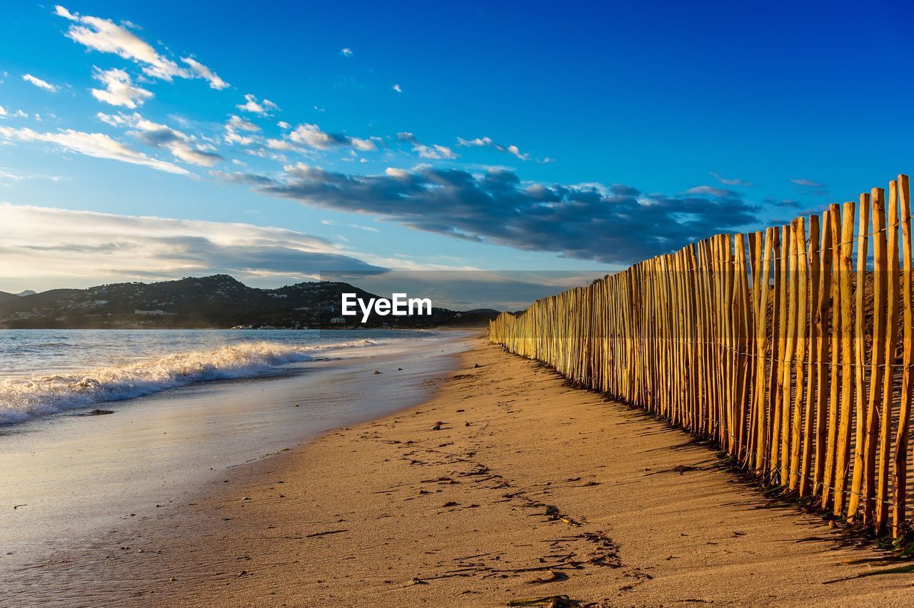 Wooden fence at beach against sky