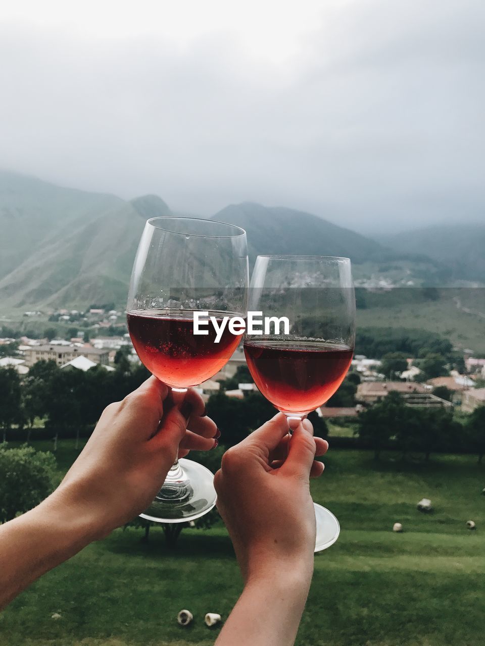 Two glasses of rose wine in two hands in fronf of mountains