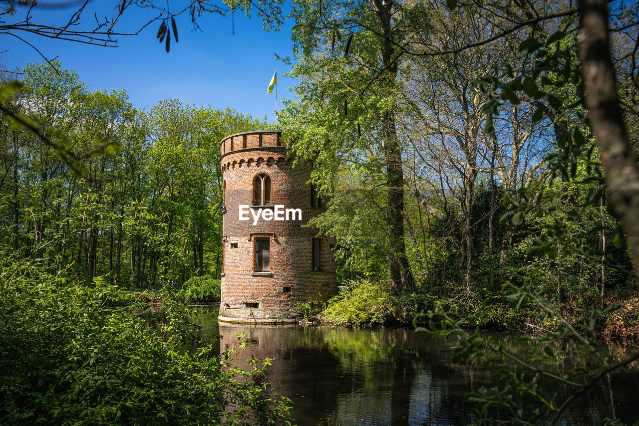 Castletower by plants in lake against sky, impressions of moated castle bladenhorst in springtime