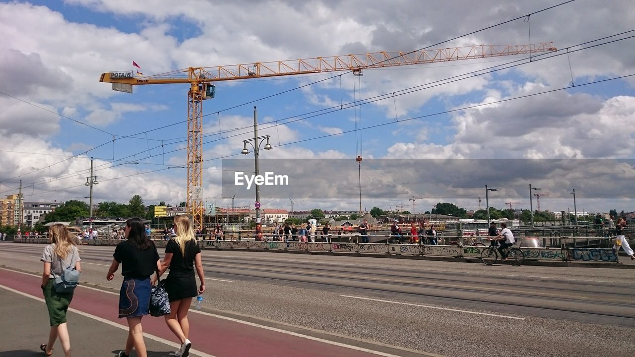 Rear view of female friends walking on road in city against sky