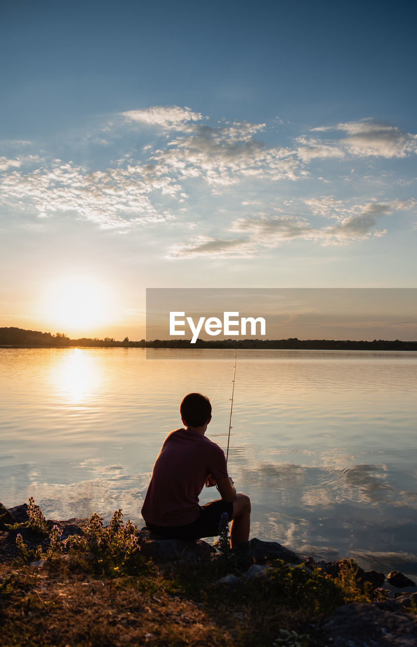 Adolescent boy fishing on shore of lake at sunset in ontario, canada.