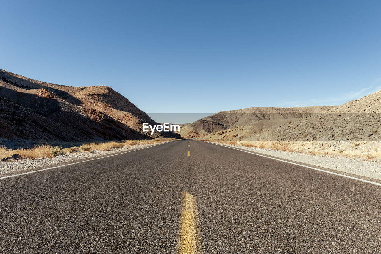 Road leading towards mountains against clear sky