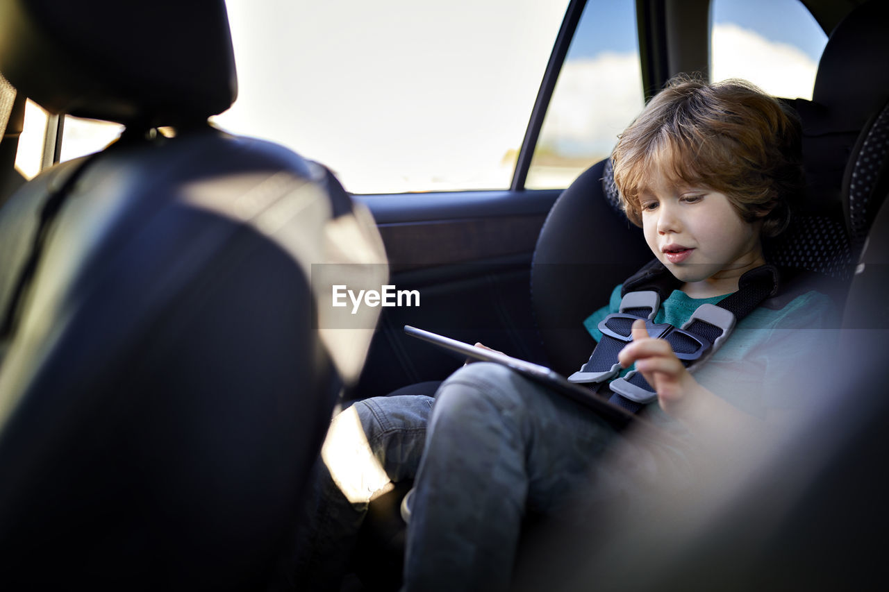Cute boy using tablet pc while traveling in car