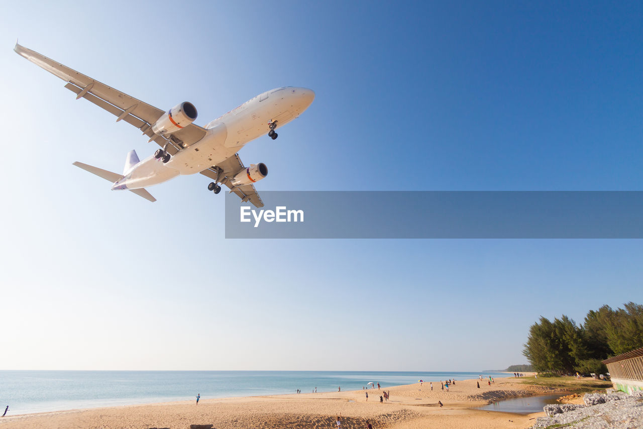 AIRPLANE FLYING OVER SEA AGAINST CLEAR SKY