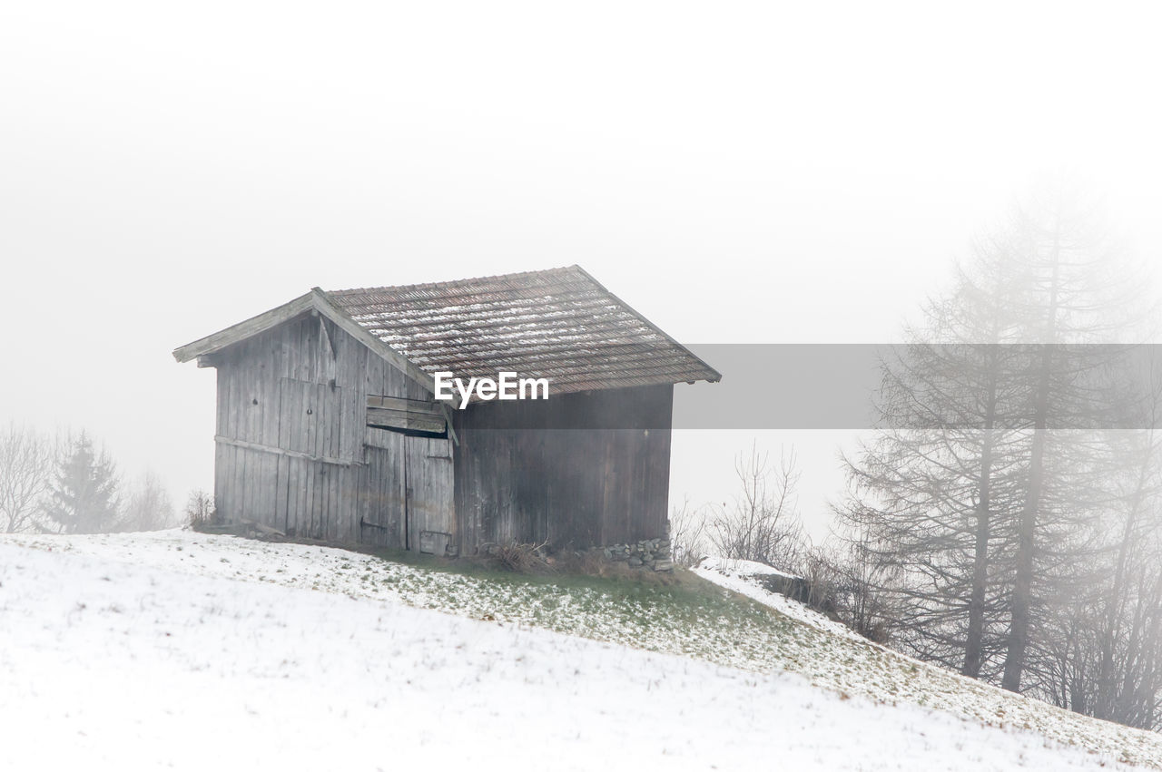 Old house on snow covered hill against sky