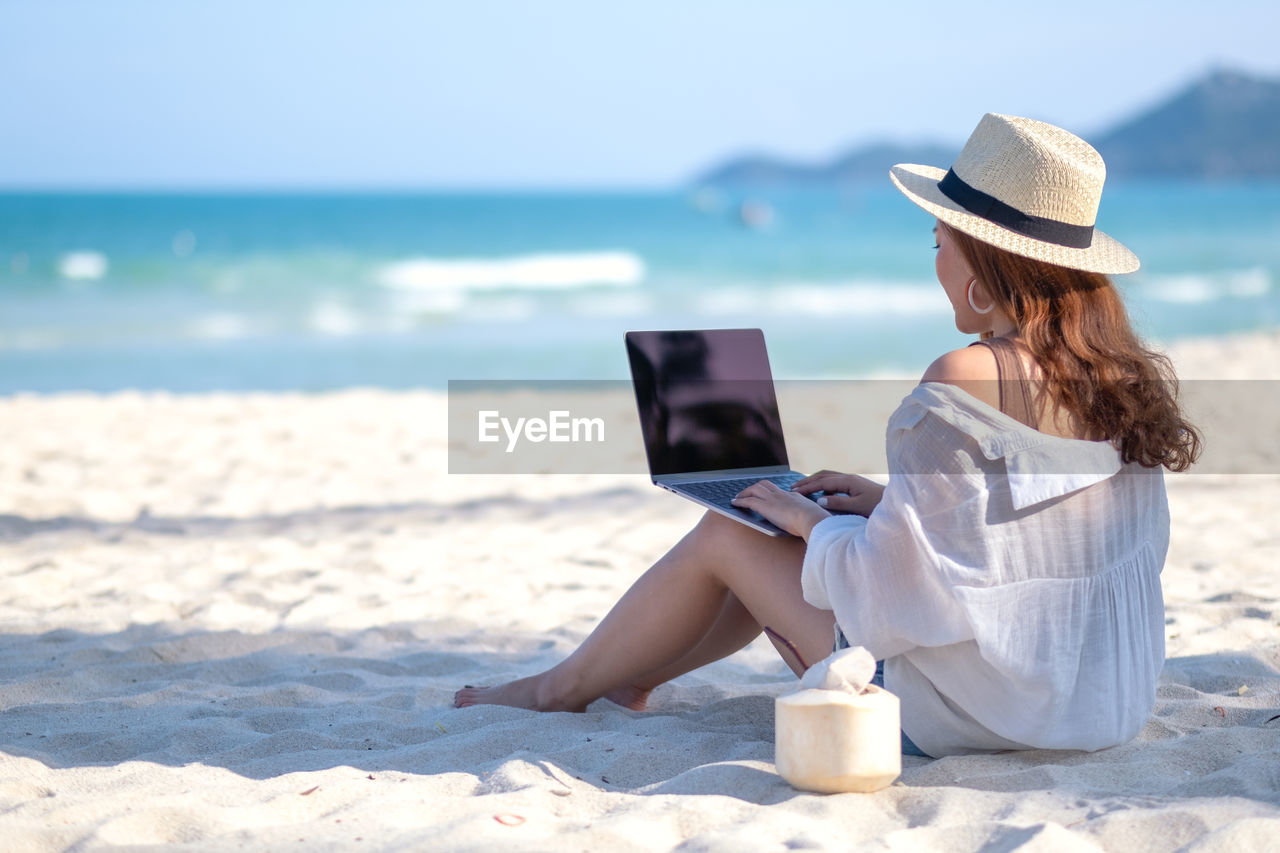Mid adult woman using laptop while sitting at beach