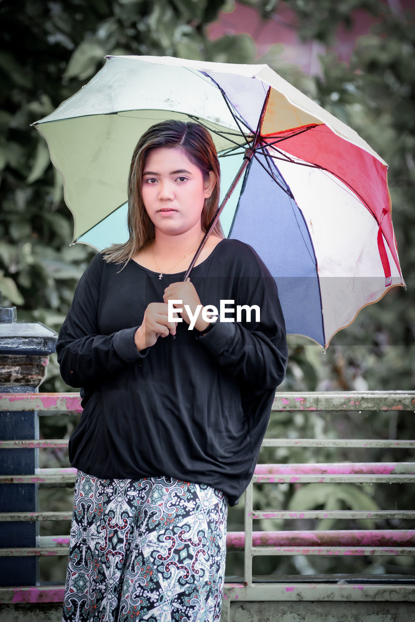 Portrait of young woman with umbrella standing outdoors