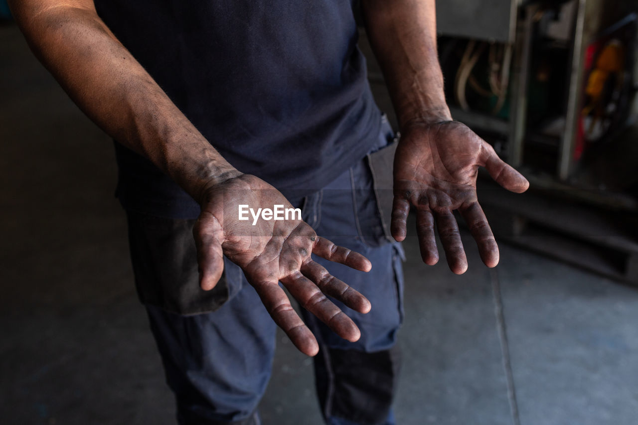 High angle of crop unrecognizable male mechanic showing dirty hands while working in repair service workshop