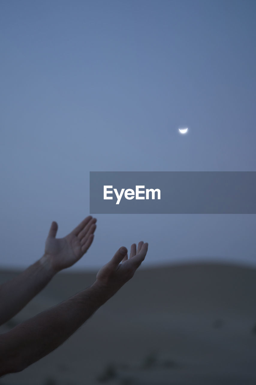 Person hand against moon in sky