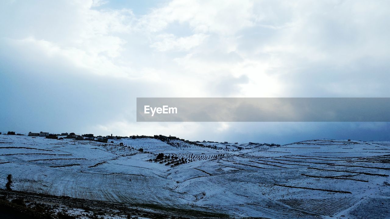 Snow covered landscape against cloudy sky