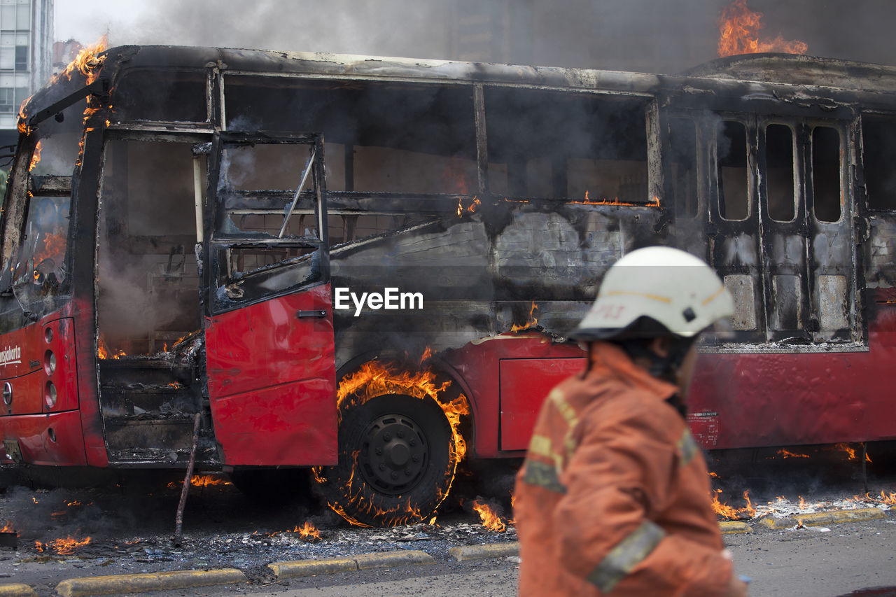 Firefighter standing by bus burning on street