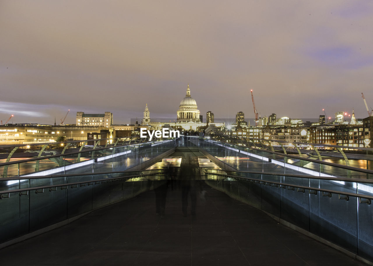 Double exposure of people on bridge against illuminated cityscape