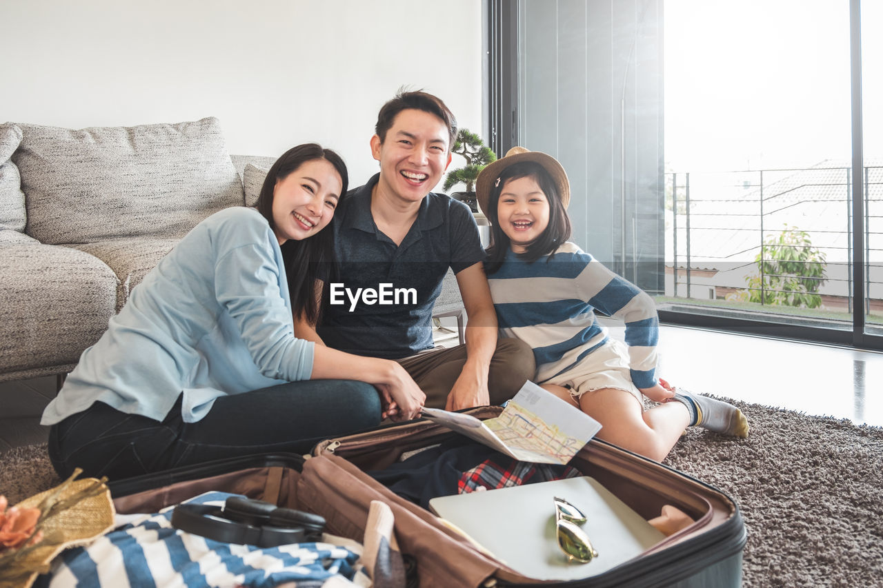 Portrait of happy family sitting by luggage at home