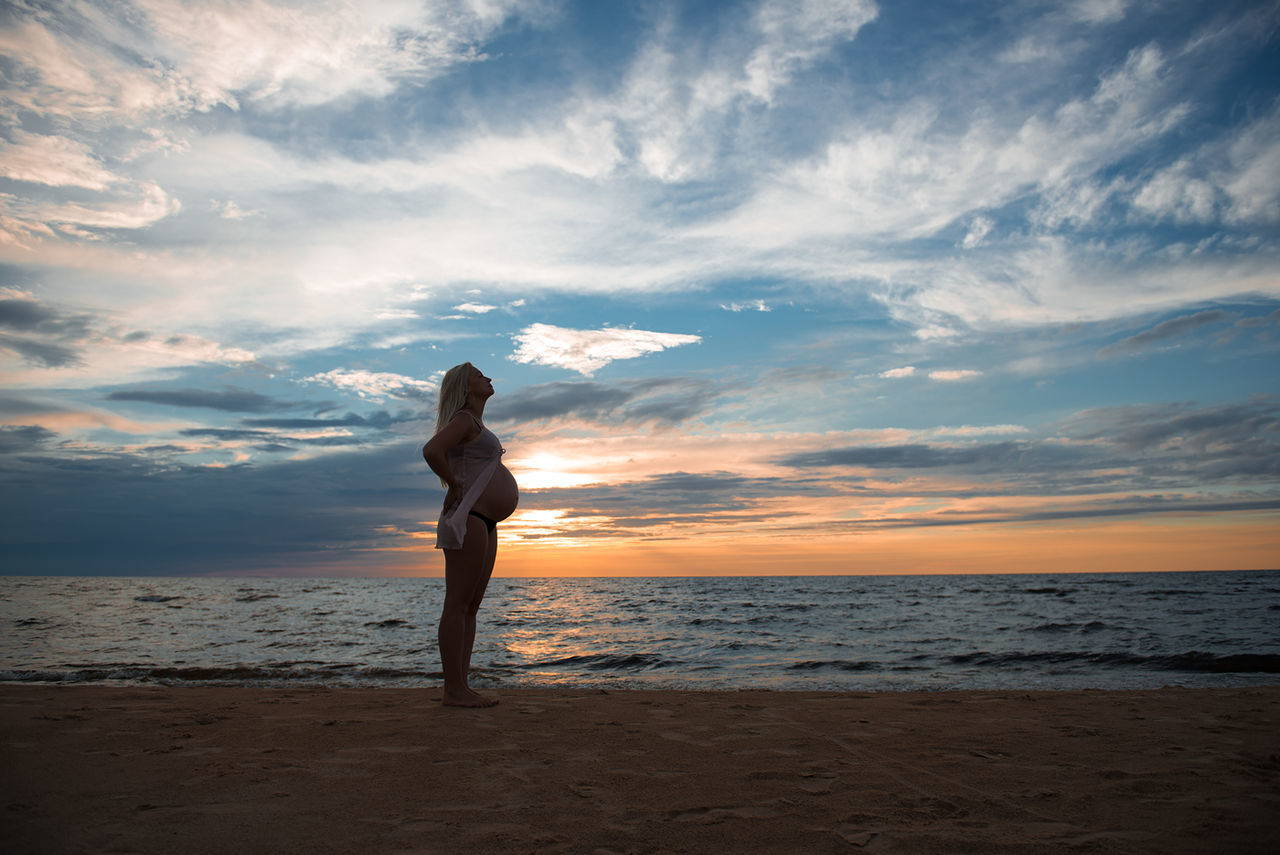 Woman standing on beach against sky during sunset