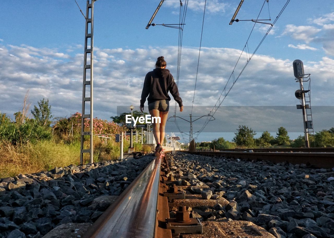 Rear view of woman standing on railroad track