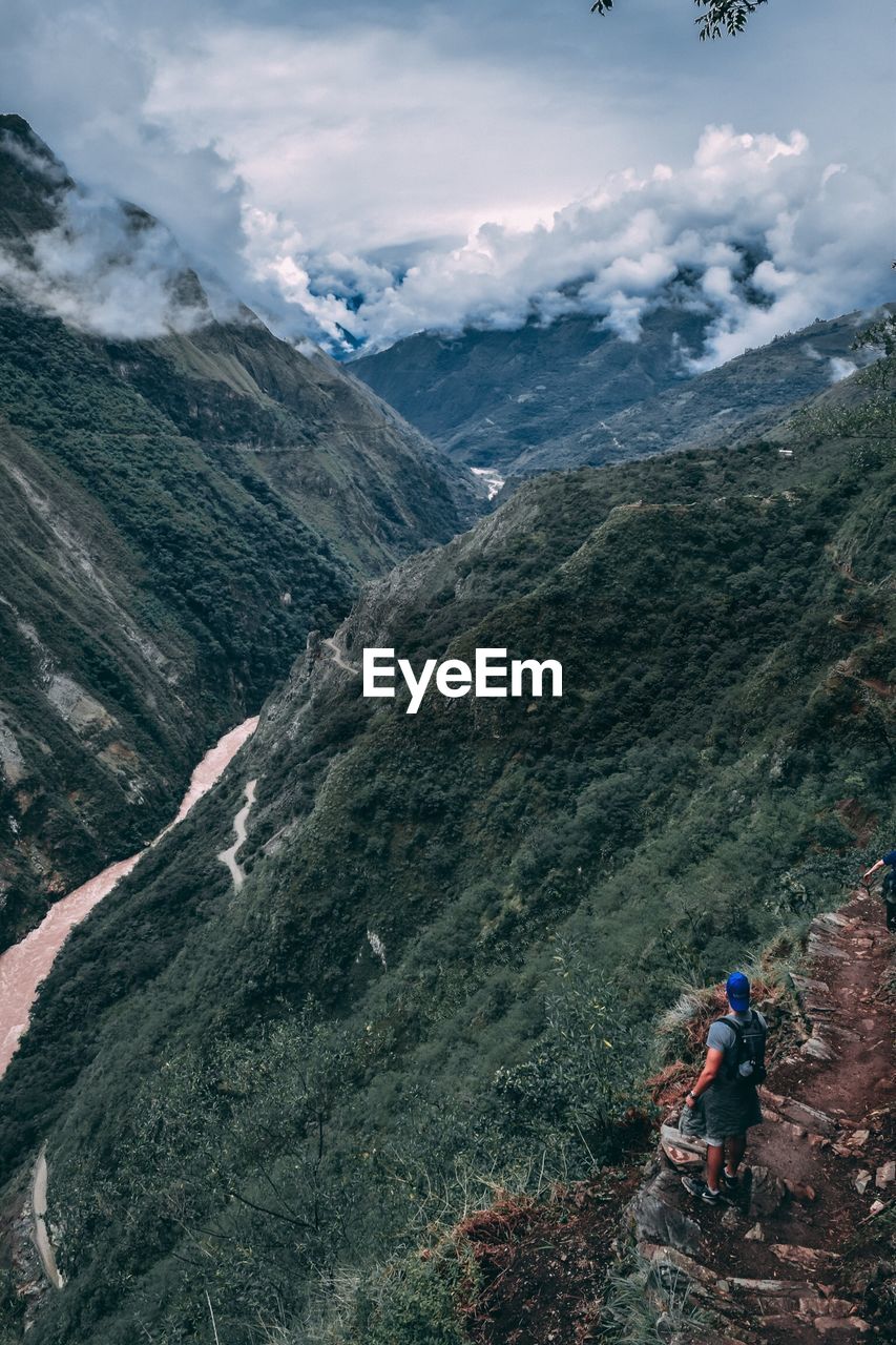 Male hiker standing on mountain against cloudy sky