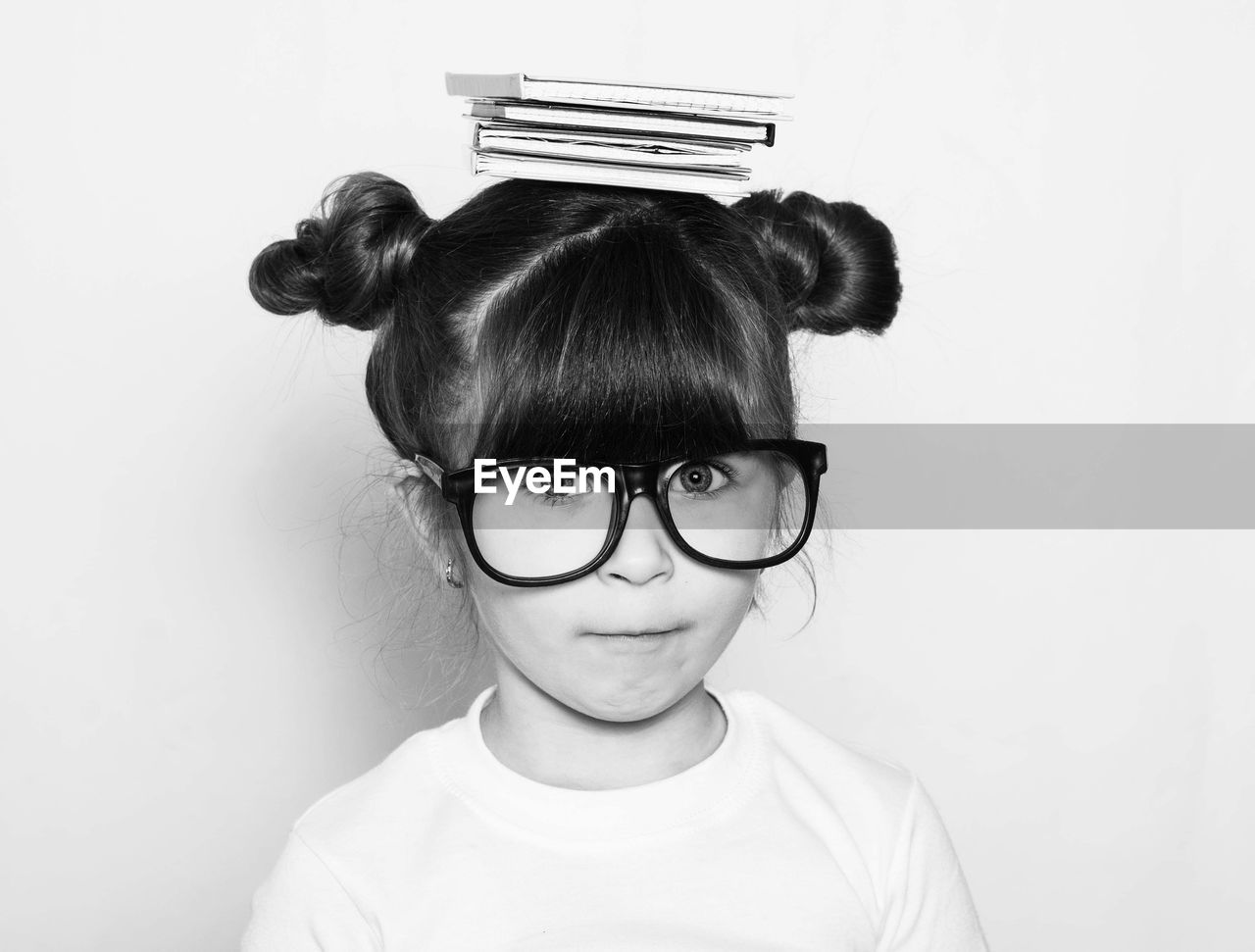 Portrait of cute nerd girl balancing books on head against white background