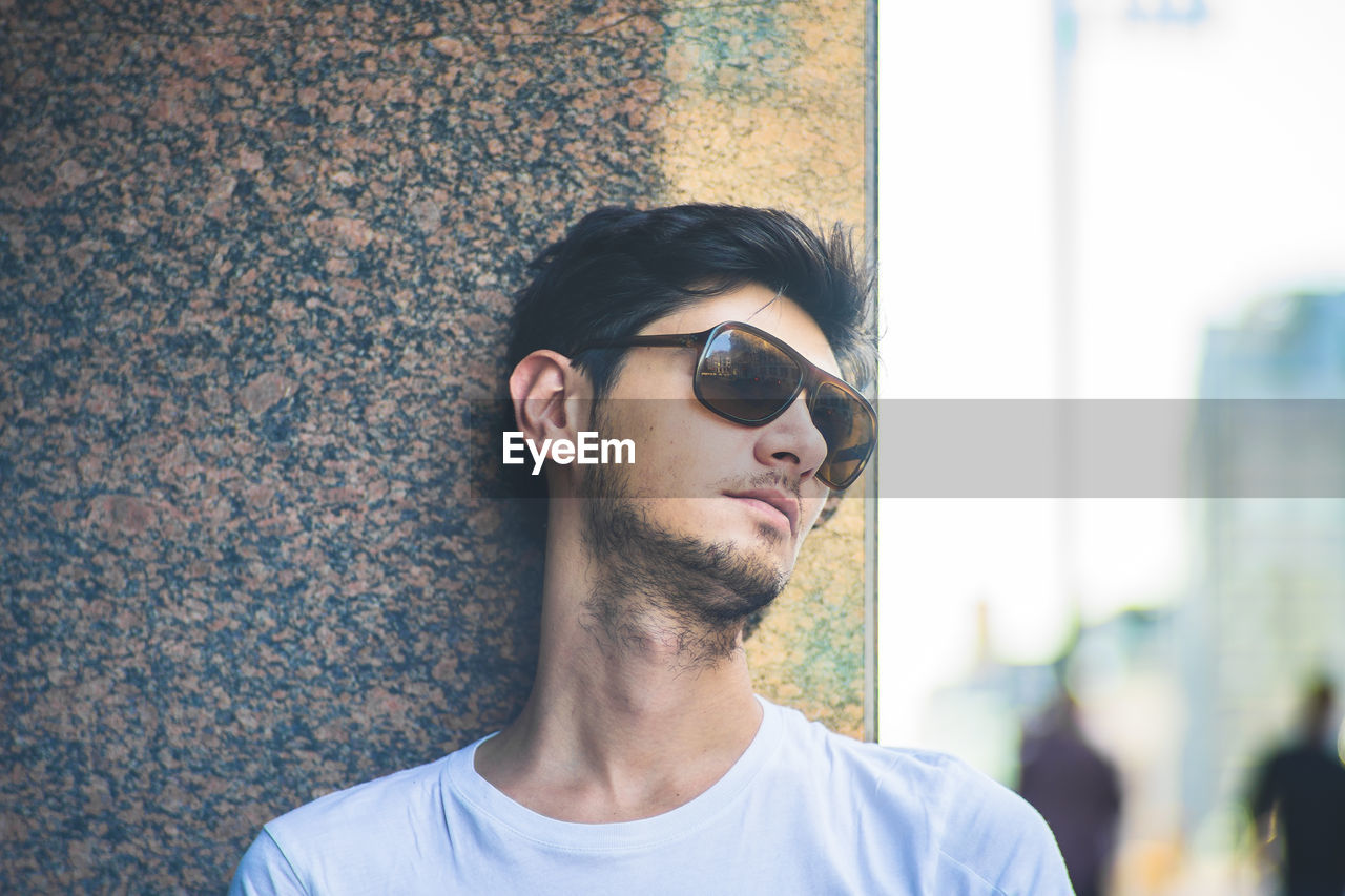 Close-up of young man wearing sunglasses standing against wall