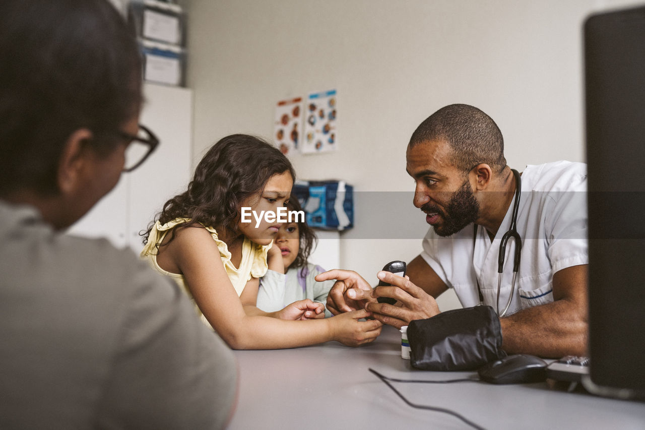 Male doctor showing glaucometer to girl in medical clinic