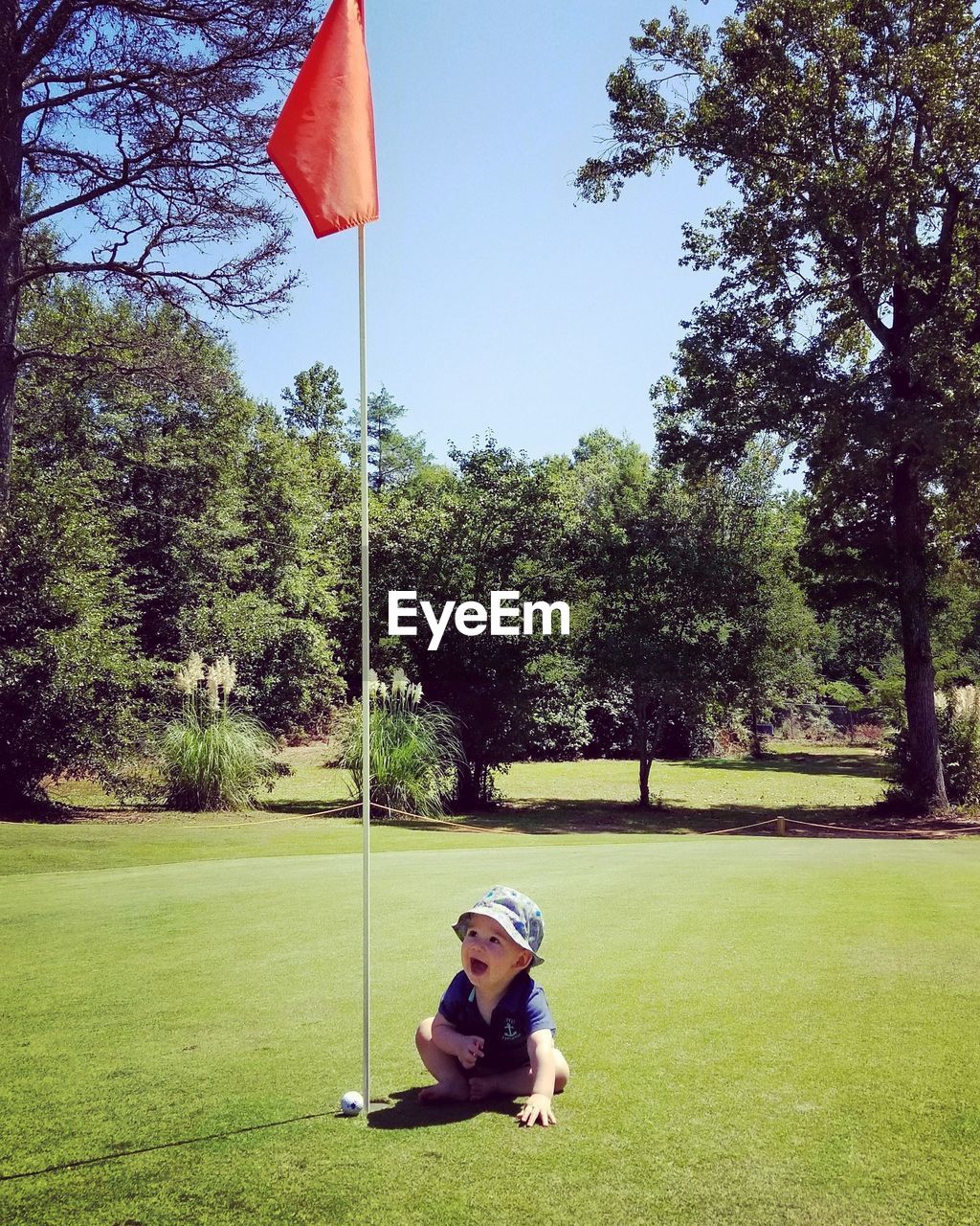 Cute baby boy sitting by golf flag on field